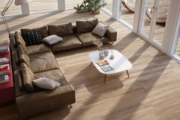 Die Ceramicvision Woodtrend Castagno Fliesen sind sowohl im Wohnzimmer als auch im Außenbereich einen modernen Lofts zu sehen. Auf dem Fliesenboden in Holzoptik ist eine kaffeebraune Couch zu sehen mit einem weißen Wohnzimmertisch. 