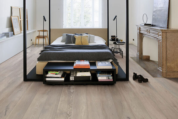 Großes Bett mitten im Schlafzimmer auf Fliesenboden in Holzoptik. Kronos Ceramiche Les Bois slavonia.