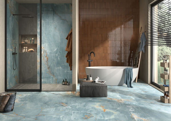 Ausschnitt eines Badezimmers, das mit der schönen Fliese The Room des Fliesenherstellers Imola Ceramica in der besonderen Farbe Onyx Aqua Blue Gold gefliest ist. Der Blick wird auf eine Dusche und danebenstehende Badewanne gelenkt. 