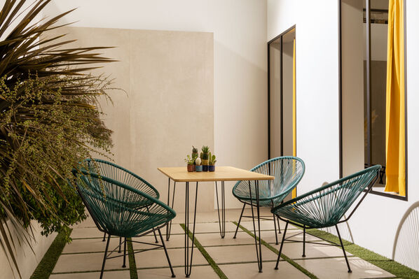Terrasse im kleinen Innenhof: Hier stehen vier Stühle an einem Tisch. Die Rückwand und der Boden der Terrasse sind in einem warmen Sandton gehalten. 