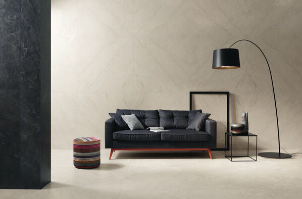 Schwarzes Sofa und schwarze Stehlampe in einem hellen Raum. Dessen Boden und Wände wurden mit Fliesen in heller Marmoroptik gestaltet – Imola Ceramica Muse. 