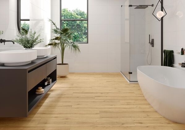 Ausschnitt eines Badezimmer, das weiße Wandfliesen und einen warmen Holzfliesen-Boden hat (Ceramicvision Concorde, Miel).