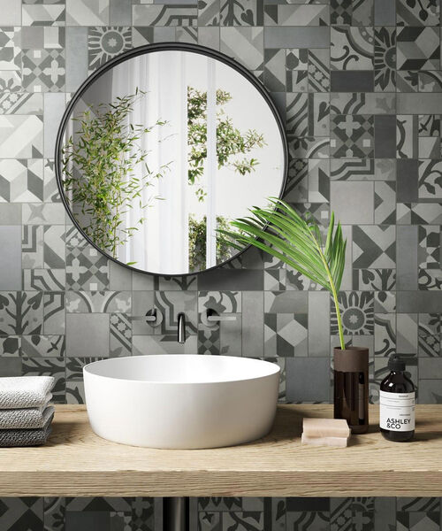 Waschtisch mit darüber hängendem runden Spiegel. Die Wand dahinter ist mit Dekorfliesen in Zementfliesenoptik gestaltet (D_Segni Blend Mosaico Carbone 19x38 cm).