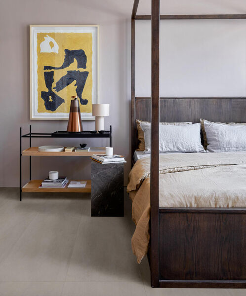 Schlafzimmer mit großem Holzbett und daneben stehendem Nachttisch. Der Fußboden ist mit der Fliese Marazzi Cementum in der Farbe Sand, 60x120 cm gestaltet.