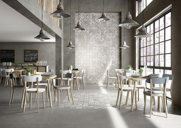Cafe in einem charmanten Industrieloft, das in grauen Farben gehalten ist. Die Wand rechts neben der Fensterfront ist mit der Dekorfliese Marazzi Block in der Farbe Grey kunstvoll in Szene gesetzt. 