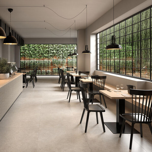 Minimalistisch eingerichtetes Cafe mit großen Fensterfronten und hellem Fußboden in Steinoptik (Marazzi Mystone Moon)