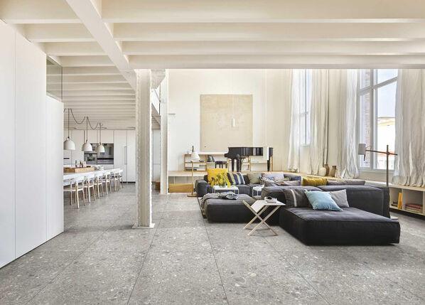 Wohnzimmer mit Loftcharakterund großen Sofa. Auf dem Fliesenboden liegt die Marazzi Mystone Ceppo di Gré.