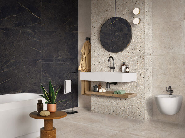 Badezimmer mit dunkel und hell gefliesten Wänden in Steinoptik. Die Wand, an der Waschbecken und Spiegel angebracht sind ist mit Fliesen im Terrazzo-Stil gestaltet. 