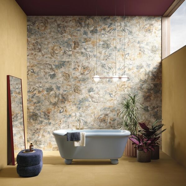 Badezimmer mit Badewanne, die vor einer Wand steht, die kunstvolle florale Muster zeigt (Del Conca Timeline Botanical), während der Boden und die seitlichen Wände mit einer sonnengelben Fliese gestaltet wurden (Del Conca Timeline Sun).