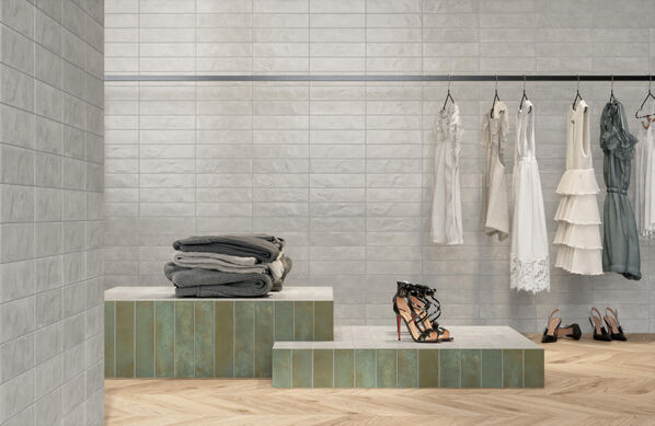 . Boutique, in der eine Kleiderstange vor einer weiß gefliesten Wand in Mauersteinoptik hängt. (Marca Corona Miniatura Fuoco). 