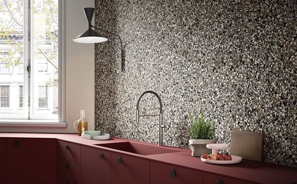 Ausschnitt einer roten Küchenzeile mit Spülbecken und einer gefliesten Wand im Terrazzostil (Del Conca Frammenti).