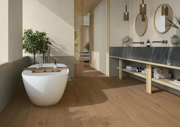 Badezimmer mit weißer Badewanne und einem großen Waschtisch. Auf dem Boden sind Fliesen in Holzoptik -Marca Corona Elisir Touch- verlegt.