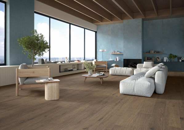 Wohnzimmer mit großen Fenstern, einer weißen Couch und einem Fußboden in Holzoptik. Gestaltet mit der Marca Corona Elisir Touch.