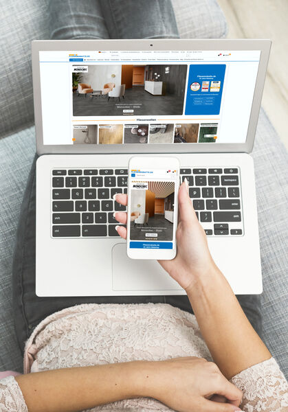 Frau sitzt mit Handy vor dem Laptop und sieht sich die Website von Fliesenrabatte.de an 