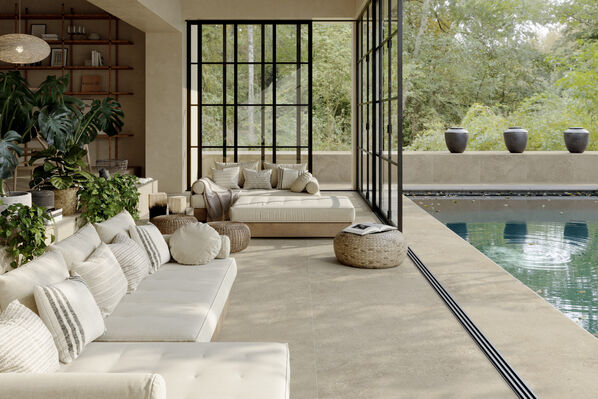 Heller Wohnraum mit Sofa, der an eine großzügige Terrasse angrenzt. Der durchgängige Fußboden in heller Natursteinoptik (Imola Ceramica Closer Beige) verbindet beide Wohnbereiche und schafft ein großzügiges Raumbild.