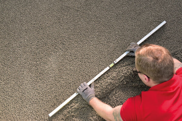 Heimwerker verteilt den Sopro SMART LeichtZuschlag mithilfe einer Ausgleichlatte.