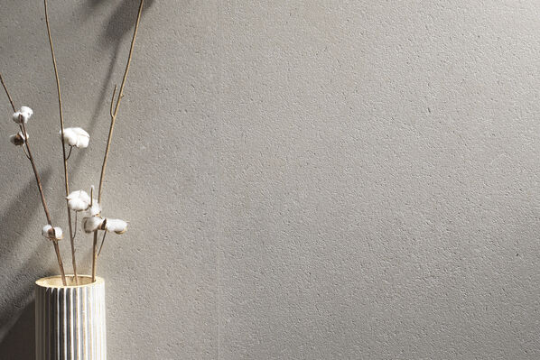 Die La Fabbica Ava Moon Cream Fliese in der Farbe Grey an der Wand mit davor stehender Vase und Blumen.