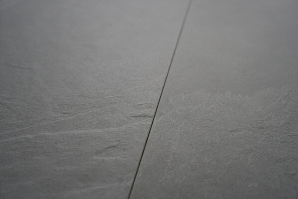Nahaufnahme der anthrazitfarbenen Fliese Ceramiche Caesar Slab2 in Schiefersteinoptik, auf der die typischen Abbruchstrukturen von Schiefer authentisch nachgebildet wurden.